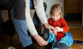 Vater hilft Kind, das am Boden sitzt, die Matschhose anzuziehen