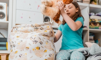 Kind räumt Kuscheltiere in einen Stoffsack, dahinter volle Regale