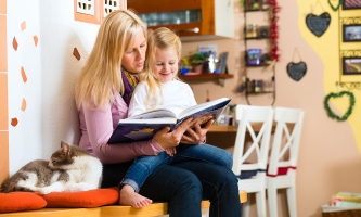 Eine Mutter hat ihre Tochter auf dem Schoß und liest ihr vor.