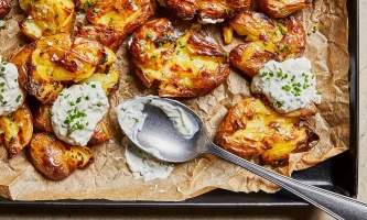 Smashed Potatoes auf einem Blech mit Schnittlauch-Dip und Löffel