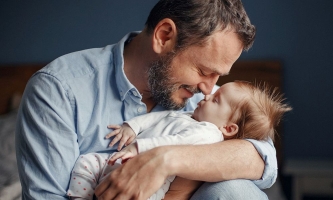 Vater hält Baby liebevoll im Arm und stupst seine Nase an die Nase des Babys.