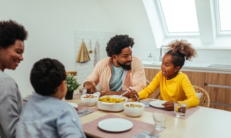 Eine Familie sitzt zusammen am Küchentisch, unterhält sich und isst.