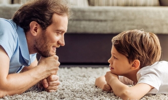 Vater und Kind liegen sich auf dem Wohnzimmerteppich gegenüber und schauen sich an