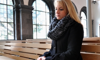 Junge Frau sitzt mit nachdenklichem Blick in Kirchenbank