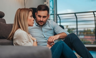 Junges Paar sitzt auf Boden vor Couch und spricht intensiv miteinander