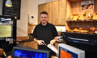 Christian Friebel steht hinter der Bäckereitheke und befüllt eine Tüte mit Ware.
