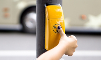 Hand eines Kindes drückt auf eine gelbe Blindenampel