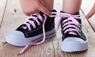 Kind bindet Schleife mit rosa Schnürsenkeln an dunkelblauen Turnschuhen