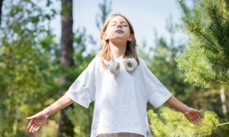 Mädchen steht versunken in Wald mit um den Hals hängenden Kopfhörern