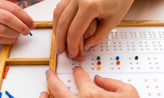 Hände eines Erwachsenen führen Kinderhände über ein Brailleboard