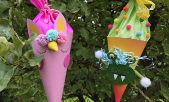 Kleine Schultüten in pink und und orange mit Augen, Zähnen und Pompons hängen in einem Baum