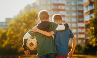 Zwei Jungen stehen vor Hochhäusern. Einer hat einen abgenutzten Fußball unter dem Arm.