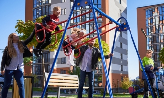Eltern schubsen Kinder auf Schaukel an, im Hintergrund moderne Hochhäuser