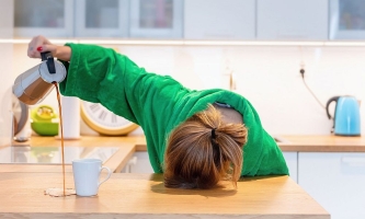 Frau liegt mit Kopf auf Arbeitsplatte in der Küche und schüttet Kaffe neben die Tasse