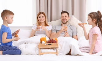 Mutter, Vater und zwei Kinder sitzen gemütlich im Ehebett und frühstücken