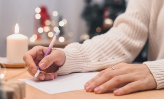 Hände von Frau mit Stift und weißem Blatt Papier, im Hintergrund Weihnachtskerzen und Lichter