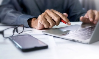 Hände tippen auf Laptop, daneben Brille und Handy