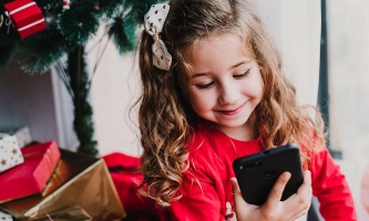 Mädchen vor Weihnachtsbaum schaut erfreut auf Handy