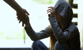 Junge Obdachlose mit Kapuze ergreift eine Hand, die ihr hingestreckt wird.