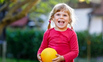 Kleines Mädchen mit Zöpfen lachend draußen mit Ball