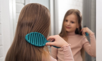 Mädchen bürstet sich vor dem Spiegel die langen dunkelblonden Haare