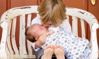 Kind küsst Baby das auf seinem Schoß liegt 