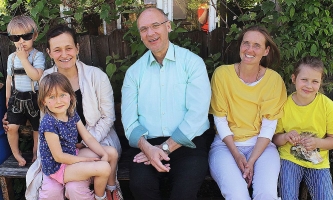 Erwachsene und Kinder sitzen im Garten auf einer Bank 