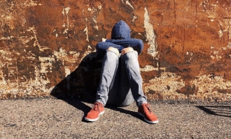 Jugendlicher mit Hoodie über dem Kopf sitzt deprimiert an Hauswand 