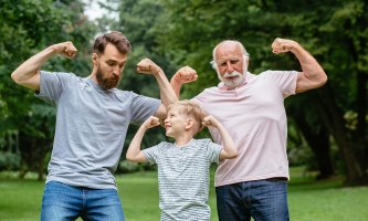 Vater, Sohn und Großvater stehen im Park und zeigen lachend ihre Muskeln