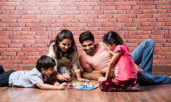 eine Familie mit zwei Kindern sitzt auf dem Boden und spielt ein Brettspiel