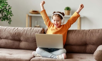 ein Mädchen sitzt mit Kopfhörern vor dem Laptop und freut sich über ein gewonnenes Videospiel