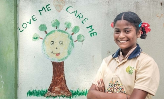 Ein Mädchen steht lachend vor einer Mauer, auf die ein Baum gemalt wurde.