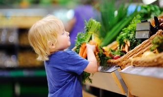 Ein Junge holt ein Bund Möhren vom Gemüsestand.