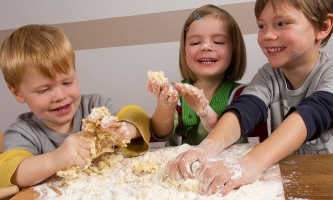 Drei Kinder beim Plätzchenbacken mit Teig an den Händen und im Gesicht 