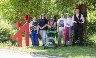 Eine Gruppe Jugendlicher steht auf der Wiese neben dem Don Bosco Logo.