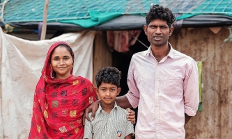 Junge glücklich mit Eltern vor Hütte in Indien 