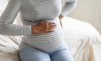 Eine Frau hält sich ihren runden Babybauch, die zweite Hand stützt den Rücken.