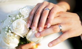 Hände von Brautpaar mit Eheringen und Brautstrauß 