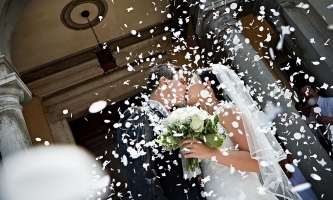 Hochzeitspaar küsst sich vor Kirche in Regen aus weißen Konfetti 