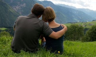 Junges Paar liebevoll aneinander angelehnt schaut auf Bergpanorama 