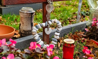 Grab mit Holzkreuz, Blumen, Herz aus Steinen und Kerze 