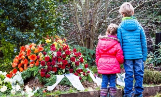 Junge und Mädchen stehen an frisch aufgeschüttetem Grab mit Kränzen 