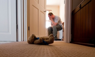 Trauernder Vater sitzt im Kinderzimmer, vor dem Zimmer liegt ein Teddybär auf dem Teppich 
