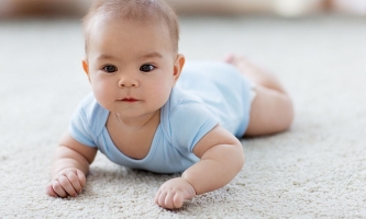 Baby im Body liegt auf Teppich und schaut interessiert 