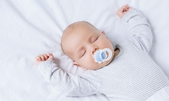 Baby im Strampelanzug mit Schnuller im Mund schlafend im Bett
