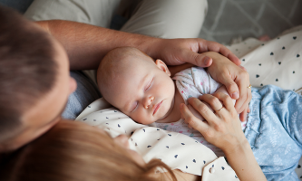 Eltern in Umarmung auf dem Sofa halten neugeborenes Baby 