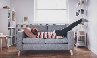 Frau liegt völlig erschöpft auf dem Sofa auf dem Bauch 