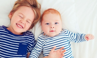 Großer Bruder liegt fröhlich mit Babybruder auf dem Bett 