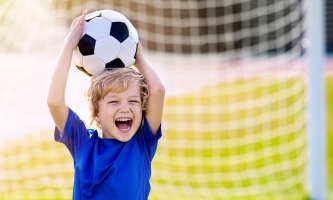 Junge auf Fußballplatz hält stolz einen Fußball in die Luft 