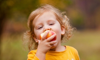 Kind in herbstilcher Natur beißt in einen Apfel 